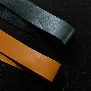 May include: Two leather straps, one black and one brown, are laid out on a dark wood surface.