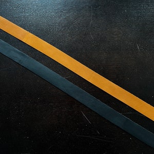 May include: Two leather straps, one black and one brown, are crossed on a dark wood surface.