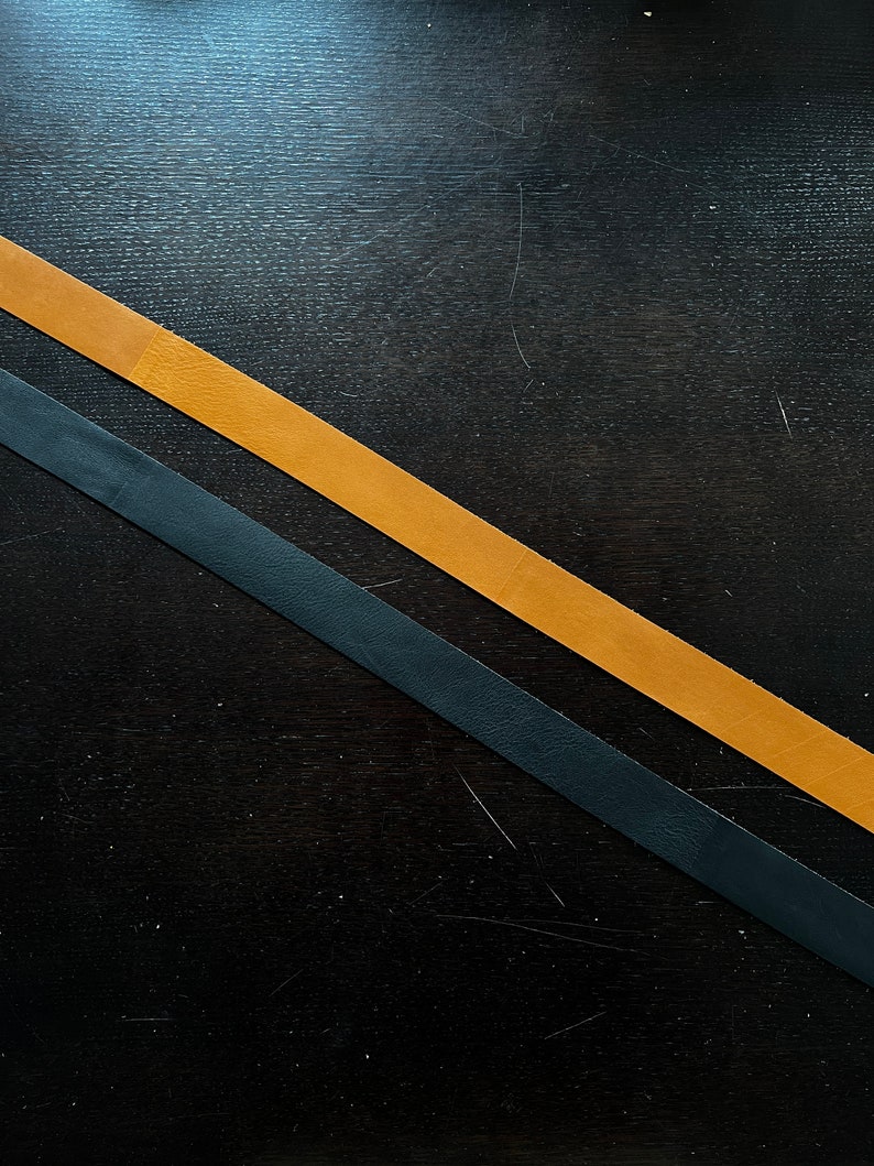 May include: Two leather straps, one black and one brown, are crossed on a dark wood surface.