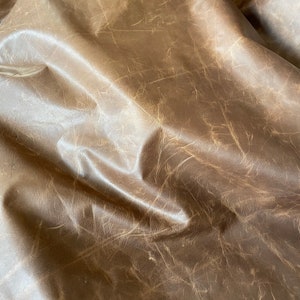 May include: Close-up of a brown leather fabric with a wrinkled texture. The leather has a light brown color and a smooth, soft feel.
