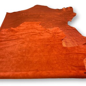 May include: A piece of orange suede leather. The leather is soft and supple, with a slightly textured surface.
