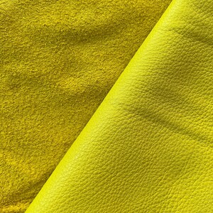 May include: Two pieces of yellow leather, one smooth and one suede, are folded over each other. The smooth leather has a textured surface.