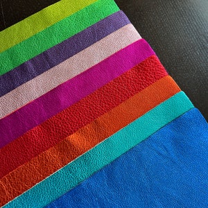 K&ouml;nnte beinhalten: Ein Stapel aus acht Lederstreifen in verschiedenen Farben, darunter Gr&uuml;n, Lila, Rosa, Magenta, Rot, Orange, T&uuml;rkis und Blau.