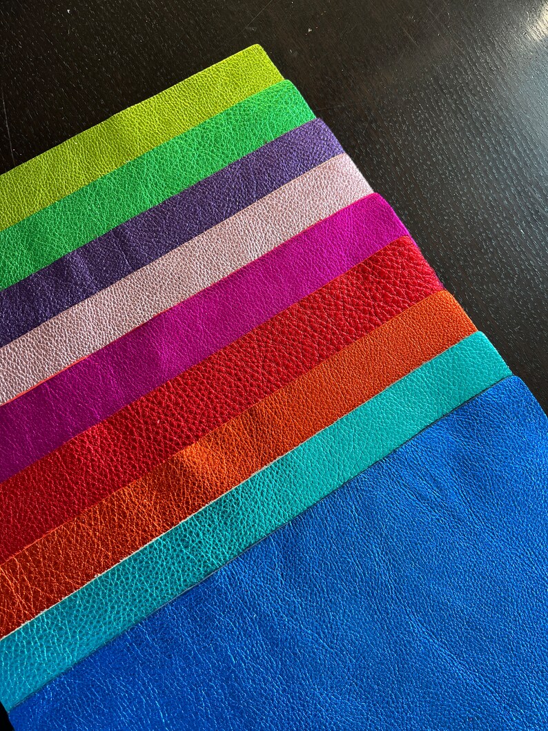 K&ouml;nnte beinhalten: Ein Stapel aus acht Lederstreifen in verschiedenen Farben, darunter Gr&uuml;n, Lila, Rosa, Magenta, Rot, Orange, T&uuml;rkis und Blau.