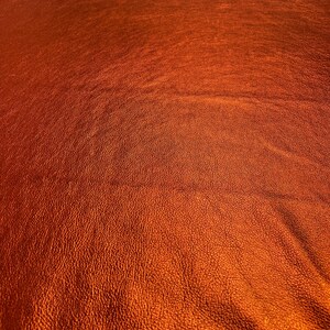 May include: Close-up of a textured, metallic orange fabric. The fabric has a subtle sheen and a slightly bumpy surface.