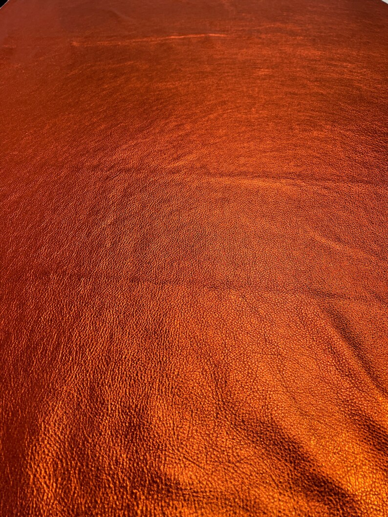 May include: Close-up of a textured, metallic orange fabric. The fabric has a subtle sheen and a slightly bumpy surface.