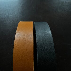May include: Two leather straps, one brown and one black, are shown side by side. The straps are both smooth and have a slight sheen.