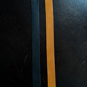 May include: Two leather straps, one black and one brown, are laid out side by side on a dark wood surface.