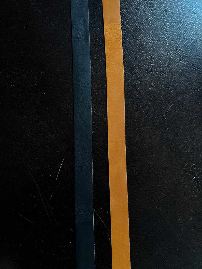 May include: Two leather straps, one black and one brown, are laid out side by side on a dark wood surface.