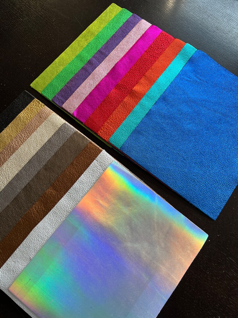 K&ouml;nnte beinhalten: Eine Sammlung von bunten Lederproben in verschiedenen Farbt&ouml;nen von Gr&uuml;n, Lila, Rosa, Rot, Orange, Blau und Braun. Die Proben sind f&auml;cherf&ouml;rmig angeordnet, wobei sich die irisierende Probe unten befindet.