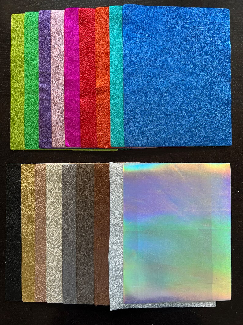 K&ouml;nnte beinhalten: Sortiment von 18 Lederproben in verschiedenen Farben und Texturen, darunter Gr&uuml;n, Lila, Pink, Rot, Orange, Blau, Schwarz, Gold, Braun, Grau und Wei&szlig;. Die Proben sind in zwei Reihen auf einer dunklen Oberfl&auml;che angeordnet.