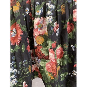 May include: A black fabric garment featuring a dense, colorful floral print. The pattern includes large red, pink, and orange blossoms, smaller yellow flowers, and clusters of tiny blue and white petals, all set against a dark background.