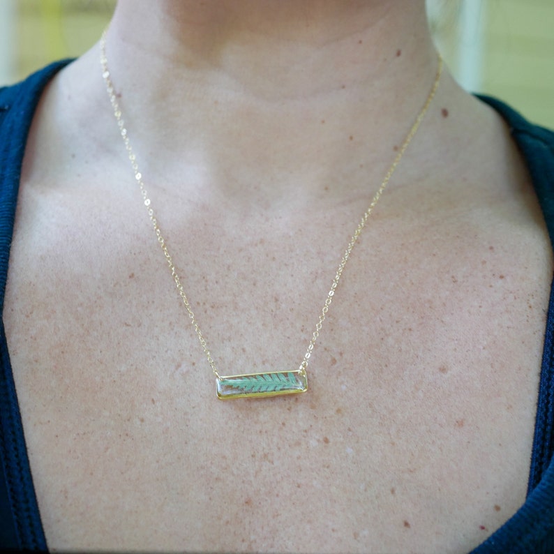 May include: A gold chain necklace with a rectangular pendant featuring a pressed green fern leaf inside clear resin.