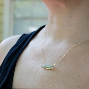 May include: A gold chain necklace with a rectangular pendant featuring a green and blue design.