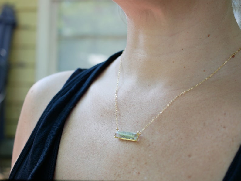 May include: A gold chain necklace with a rectangular pendant featuring a green and blue design.