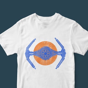 Pode incluir: Camiseta branca com um gráfico azul e laranja de um caça TIE. O design é centrado, com as asas do caça se estendendo. O gráfico tem um visual vintage e desgastado.