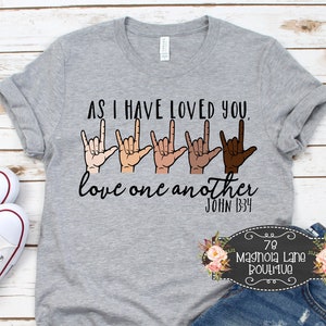 May include: Gray t-shirt with the text "AS I HAVE LOVED YOU, love one another JOHN 13:34" and a row of hands in different skin tones signing the word "love" in American Sign Language.