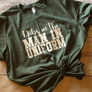 May include: A green t-shirt with the text "Dibs on the man in uniform" printed in white.
