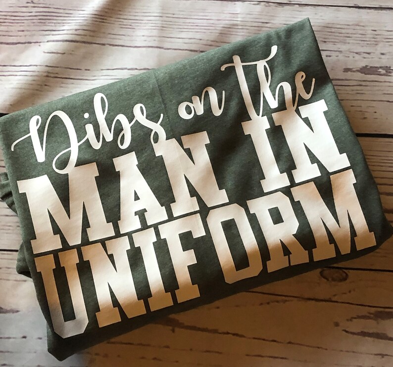 May include: A green t-shirt with white text that reads "Dibs on the man in uniform".