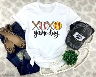 May include: White t-shirt with a graphic of two crossed baseball bats and two baseballs with the text "XOXO game day".