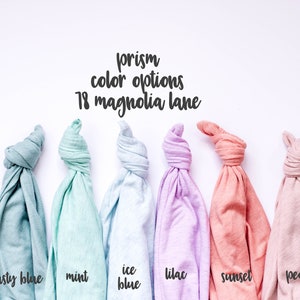 May include: Six folded t-shirts in different pastel colours: dusty blue, mint, ice blue, lilac, sunset, and peach. The text "prism colour options 18 magnolia lane" is above the shirts.