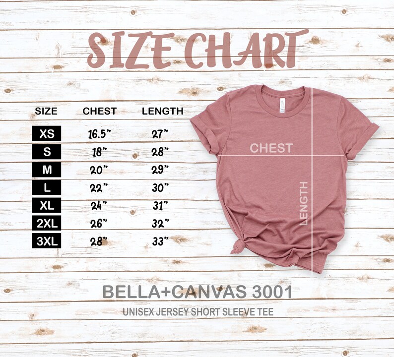 May include: Size chart for a unisex jersey short sleeve tee, showing chest and length measurements in inches for sizes XS to 3XL. The chart is on a woodgrain background with a pink t-shirt laid out on top.