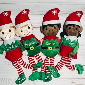 May include: Four plush elf ornaments with red and white striped legs and green elf suits. Each elf has a different name embroidered on their suit: London, Benjamin, Carter, and Jen. The elves are all wearing Santa hats with snowflakes on them.