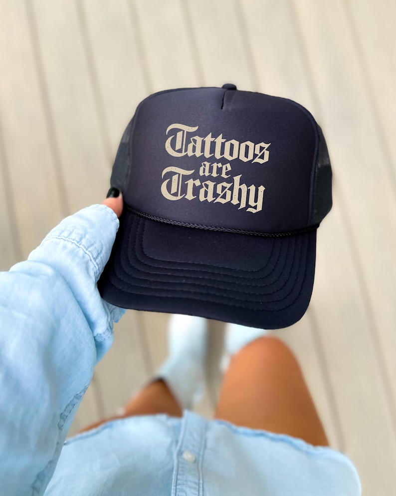 May include: Navy blue trucker hat with the text "Tattoos are Trashy" in a vintage font. The hat has a mesh back and a curved brim. A stylish accessory for anyone who loves tattoos.