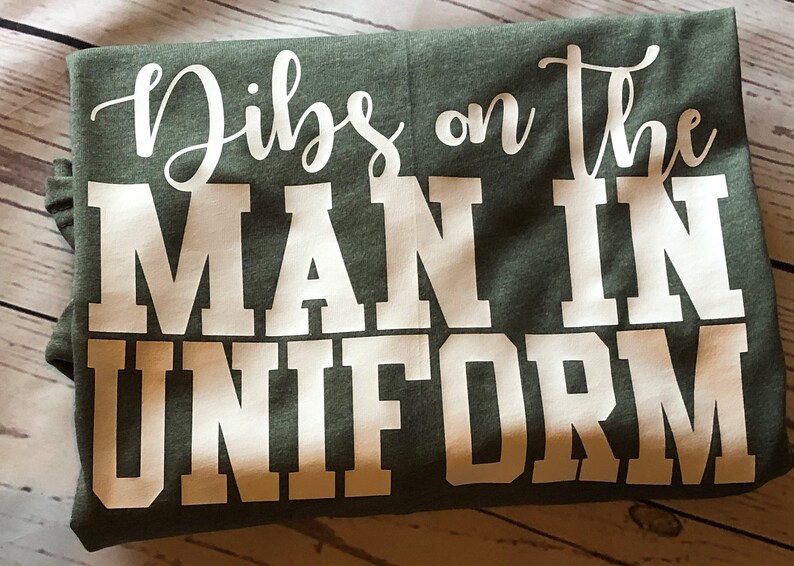 May include: A green t-shirt with white text that reads "Dibs on the Man in Uniform".