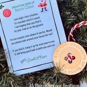 May include: A wooden button ornament with the text "Property of Santa Claus Believe" and a red and white string attached. The ornament is on a green wreath with a note from Santa Claus that reads "Last night I lost a button, it's wooden and it's round. I am hoping that you find it, by your tree or on the ground. I'm not exactly sure where it can be. Would you please look around your house for me? If you find it, hang it up for everyone to see. It will bring good luck to both you and me! Love, Santa Claus."