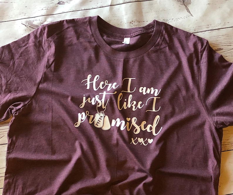 May include: Burgundy t-shirt with the text "Here I am just like I promised xxx" in gold lettering. Two gold dog tags with the word "HITT" on them are hanging from a chain above the text.