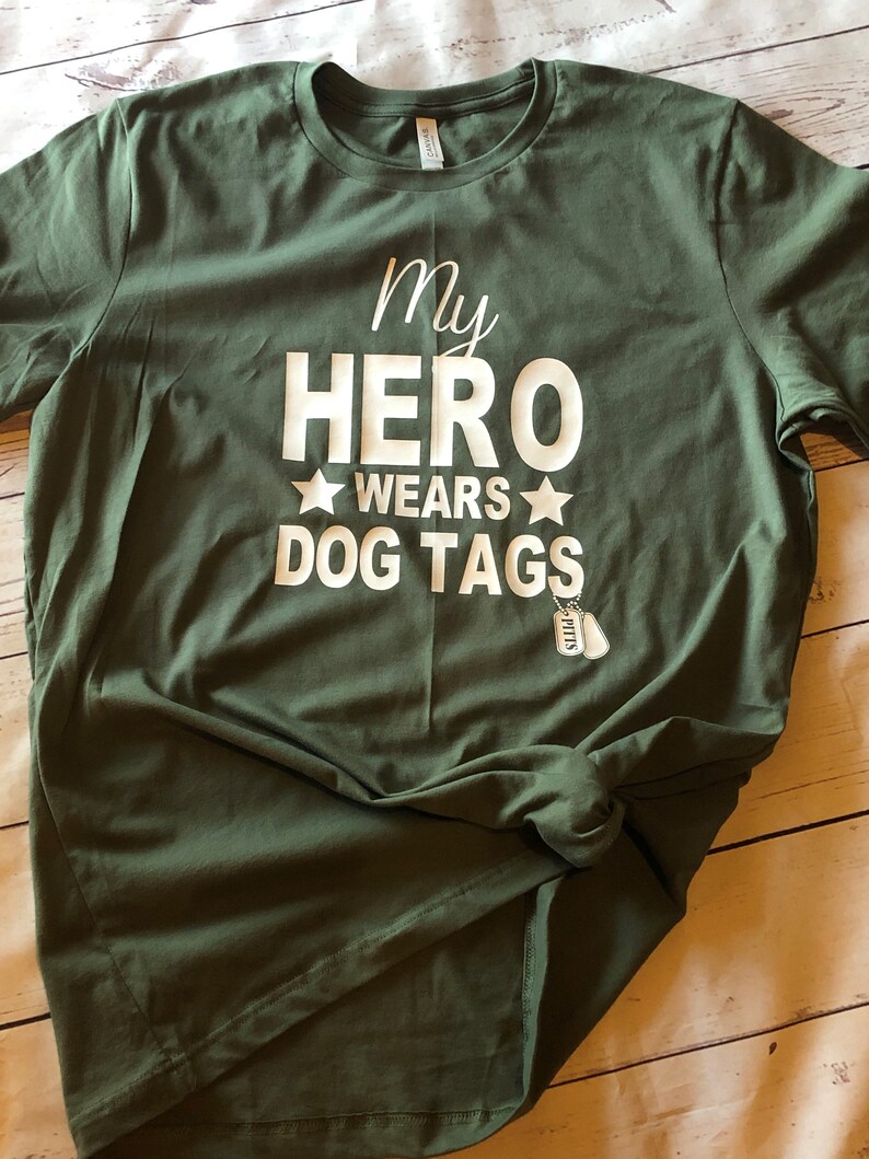 May include: Green t-shirt with white text that reads "My Hero Wears Dog Tags" with a small silver dog tag charm.