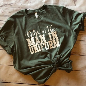 May include: A green t-shirt with the text "Dibs on the man in uniform" printed in white.