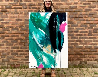 May include: A woman holds a large abstract painting with bold strokes of black, green, and pink paint on a white canvas.
