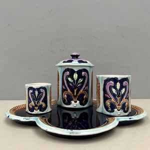 Peut inclure: Un ensemble de vanité en céramique avec un plateau, un pot à couvercle et deux tasses. L'ensemble présente un motif floral turquoise, bleu marine et or. Le plateau et les tasses ont une texture tissée.