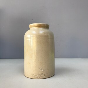 Op de afbeelding: Een witte keramische pot met een inhoud van 1L. De pot heeft een eenvoudig ontwerp met een gladde, geglazuurde afwerking. De onderkant van de pot heeft een label met de tekst "1L" en "Emma Brookes Weight".