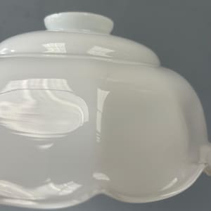 May include: A white milk glass lamp shade featuring a smooth, rounded dome shape with a scalloped edge at the bottom. The glass has a glossy, reflective surface with a circular opening at the top for mounting, showcasing a classic, curved design.