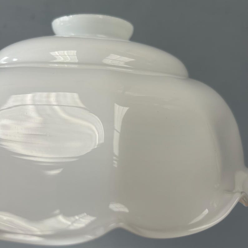 May include: A white milk glass lamp shade featuring a smooth, rounded dome shape with a scalloped edge at the bottom. The glass has a glossy, reflective surface with a circular opening at the top for mounting, showcasing a classic, curved design.