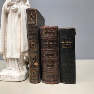 May include: Three antique books with black leather covers and gold lettering. The titles are "Les Gloires de Marie", "Paroissien Latin-Français", and "Paroissien d'Evreux Texte Latin".