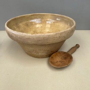 May include: A large, off-white ceramic bowl with a slightly rough texture and a wooden spoon. The bowl is slightly chipped on the rim.