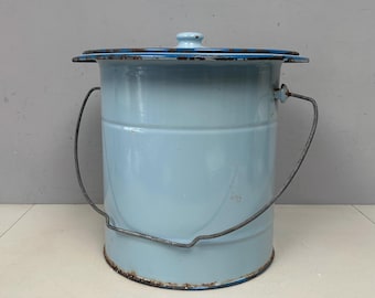 May include: A light blue enamelware bucket with a lid and a metal handle. The bucket has a cylindrical shape with a slightly flared rim. The lid is also light blue with a dark blue rim. The handle is made of metal. The bucket shows signs of wear.