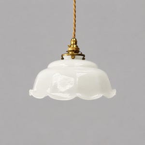May include: A white glass pendant light fixture with a scalloped edge, featuring a brass-colored metal socket and a twisted tan fabric cord. The shade has a smooth, glossy finish and a wide, rounded shape that flares outward at the bottom rim.