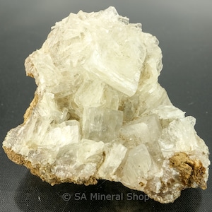 May include: A cluster of clear, white, translucent crystals on a brown rock. The crystals are arranged in a layered, stacked formation.