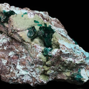 May include: A rough, dark brown rock with green and blue crystals embedded in it. The crystals are clustered together and have a shiny, metallic appearance.