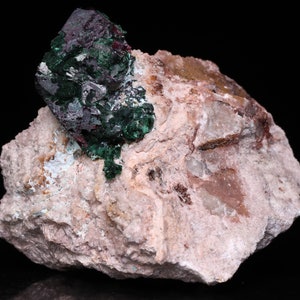 May include: A cluster of green and purple malachite crystals on a pink and white matrix. The crystals are sharp and well-defined, and the matrix is rough and textured.