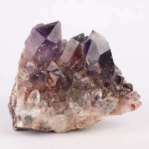 May include: A cluster of amethyst crystals with a purple hue, set in a matrix of clear quartz crystals. The crystals are arranged in a natural formation, with some pointing upwards and others pointing downwards. The amethyst crystals are translucent and have a slight shimmer.