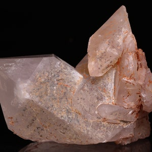 Puede incluir: Un grupo de cristales de cuarzo transparentes con un tono rosado e inclusiones marrones. Los cristales están agrupados en una formación natural.