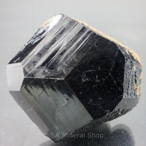 May include: A large, black, faceted, and highly reflective crystal with a geometric shape. The crystal has a smooth, polished surface and appears to be a natural mineral.