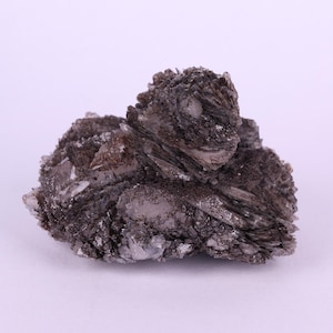 May include: A dark grey mineral specimen with layered, crystalline structures. The rock formation has a rough, textured surface with areas of lighter grey and white. The overall shape is irregular and organic, suggesting a natural, unpolished state.