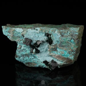 Puede incluir: Una roca rugosa de color verde oscuro y azul con un bolsillo de cristales blancos y cristales negros.